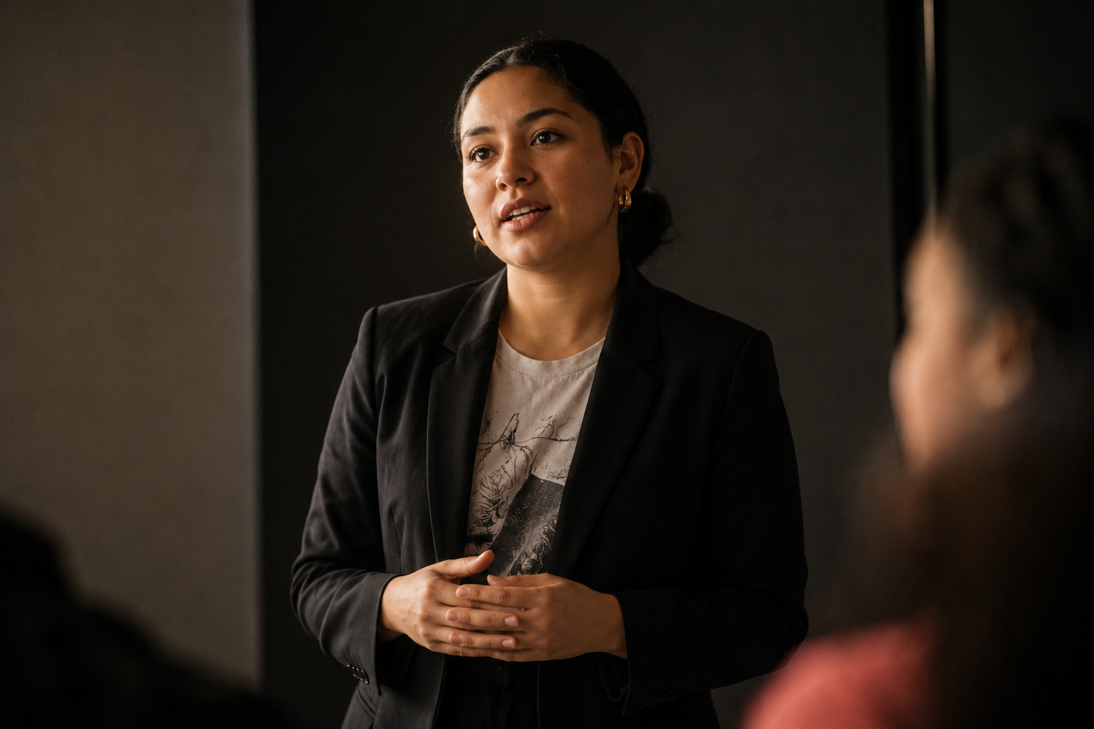 A professional woman in a black blazer speaking with intention to an audience